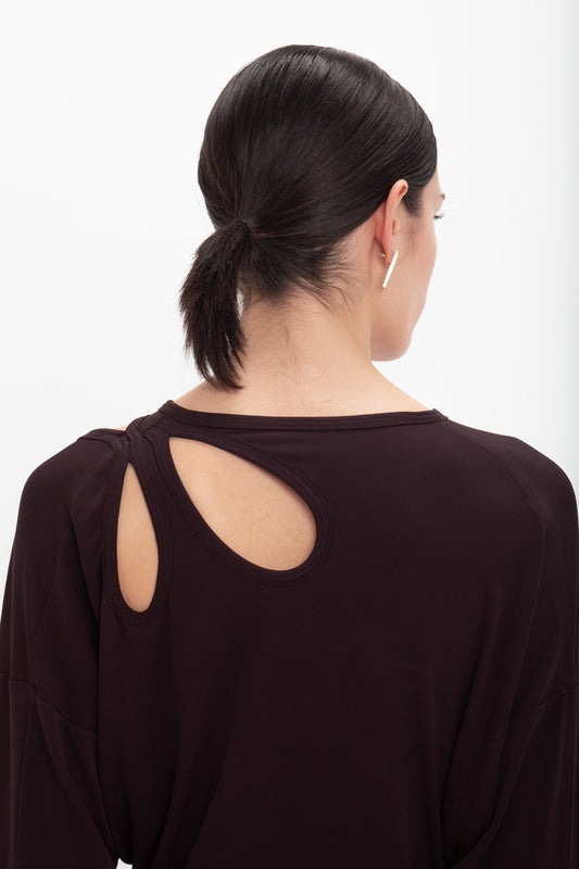 Woman from behind wearing a deep mahogany Twist Detail Jersey Top by Victoria Beckham with a circular cutout, her hair styled in a low ponytail.