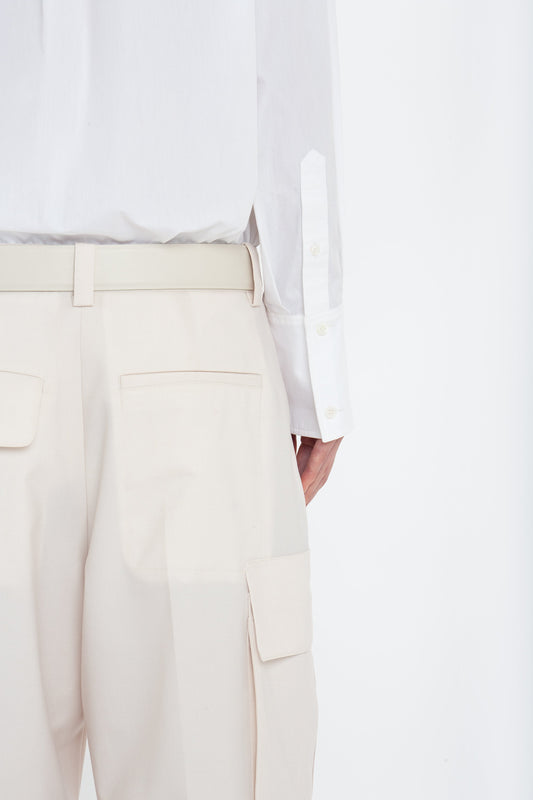 Back view of a person wearing a white shirt tucked into beige, military-inspired Relaxed Cargo Trouser In Bone by Victoria Beckham with a belt. The 100% cotton pants feature back pockets and a side cargo pocket.