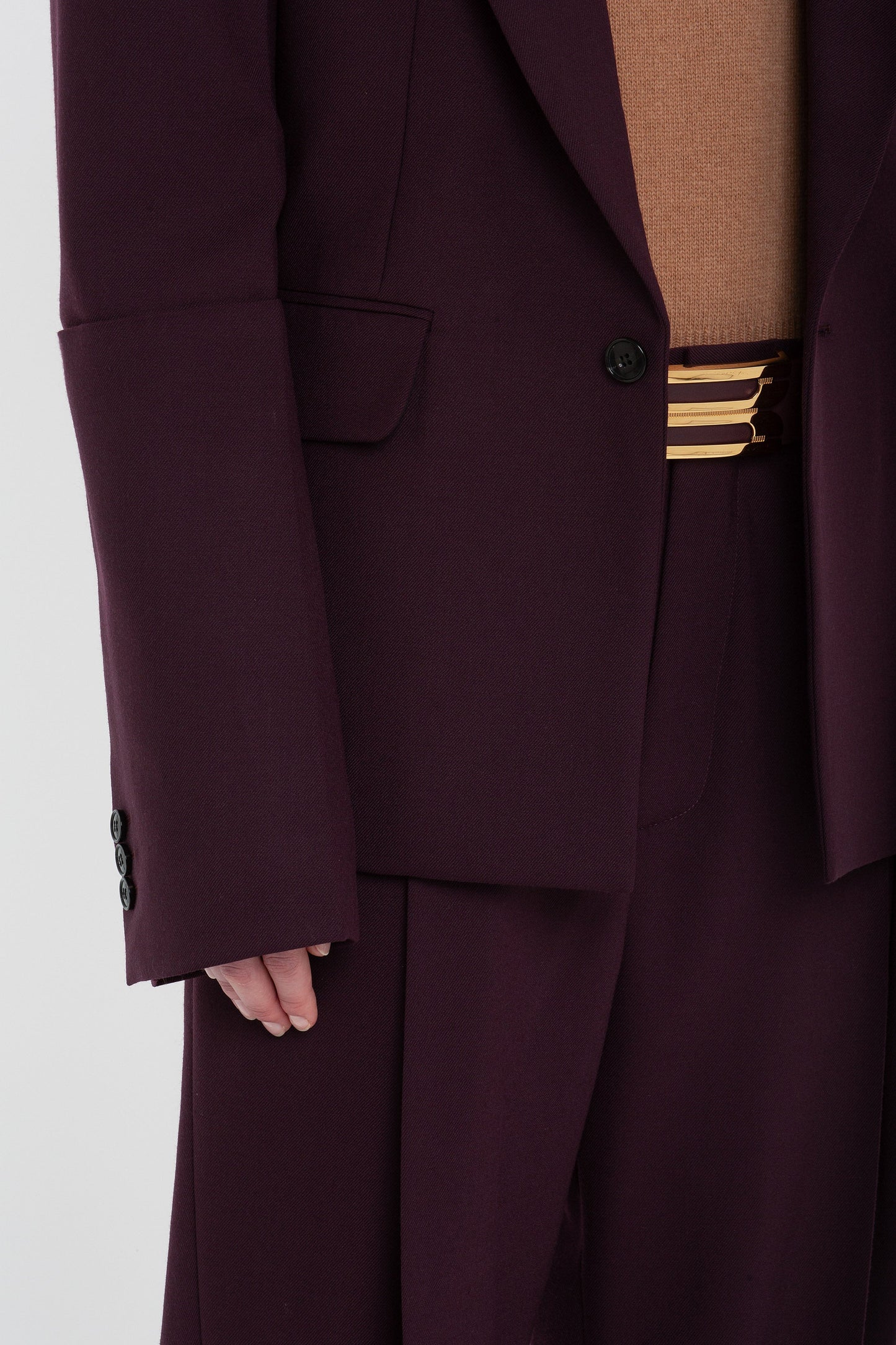 Close-up of a person wearing a Sleeve Detail Patch Pocket Jacket In Deep Mahogany by Victoria Beckham, tan shirt, and maroon trousers with a unique triple-striped belt.