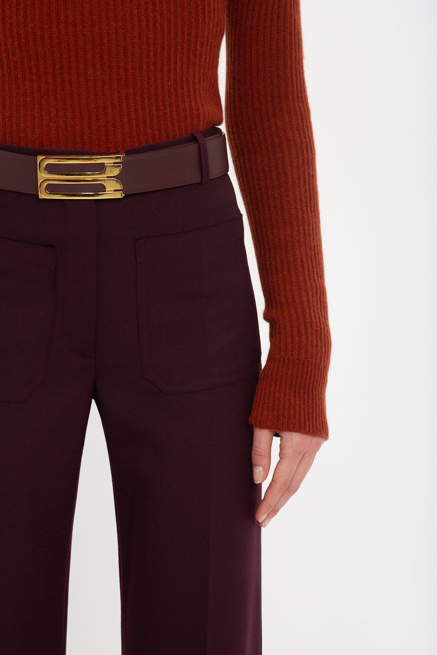 A person wearing a Victoria Beckham Double Collared Jumper In Russet and burgundy trousers with a matching belt, standing against a plain white background.