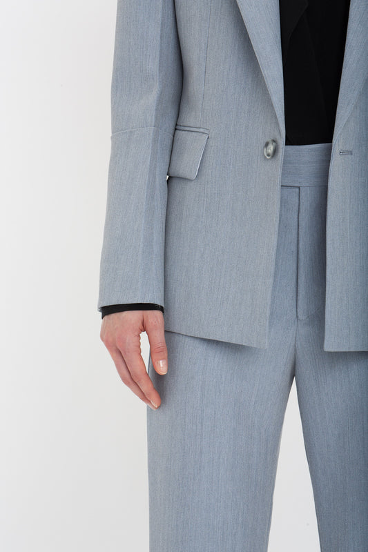 A person wearing an impeccably tailored light gray suit with a black shirt underneath, featuring the Exclusive Sleeve Detail Patch Pocket Jacket In Marina by Victoria Beckham, shown from the neck to the knee against a white background.
