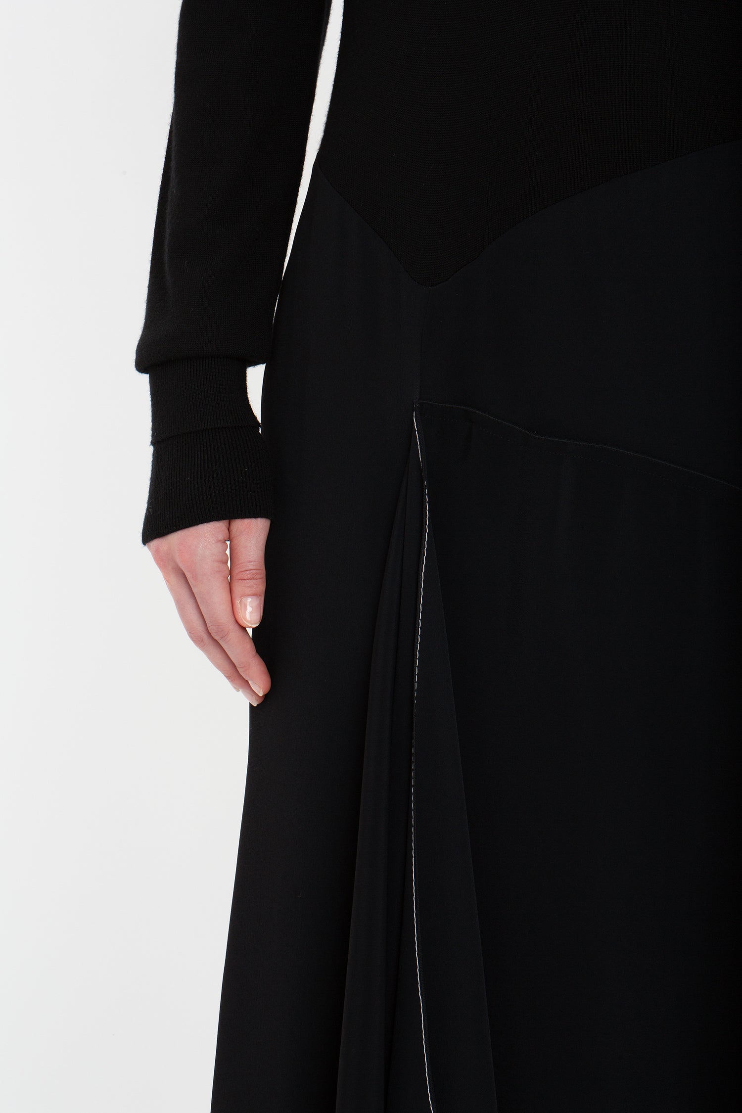 A person wearing a Henley Shirt Dress In Black by Victoria Beckham, featuring an asymmetric waist seam, shown from the neck down to mid-thigh.