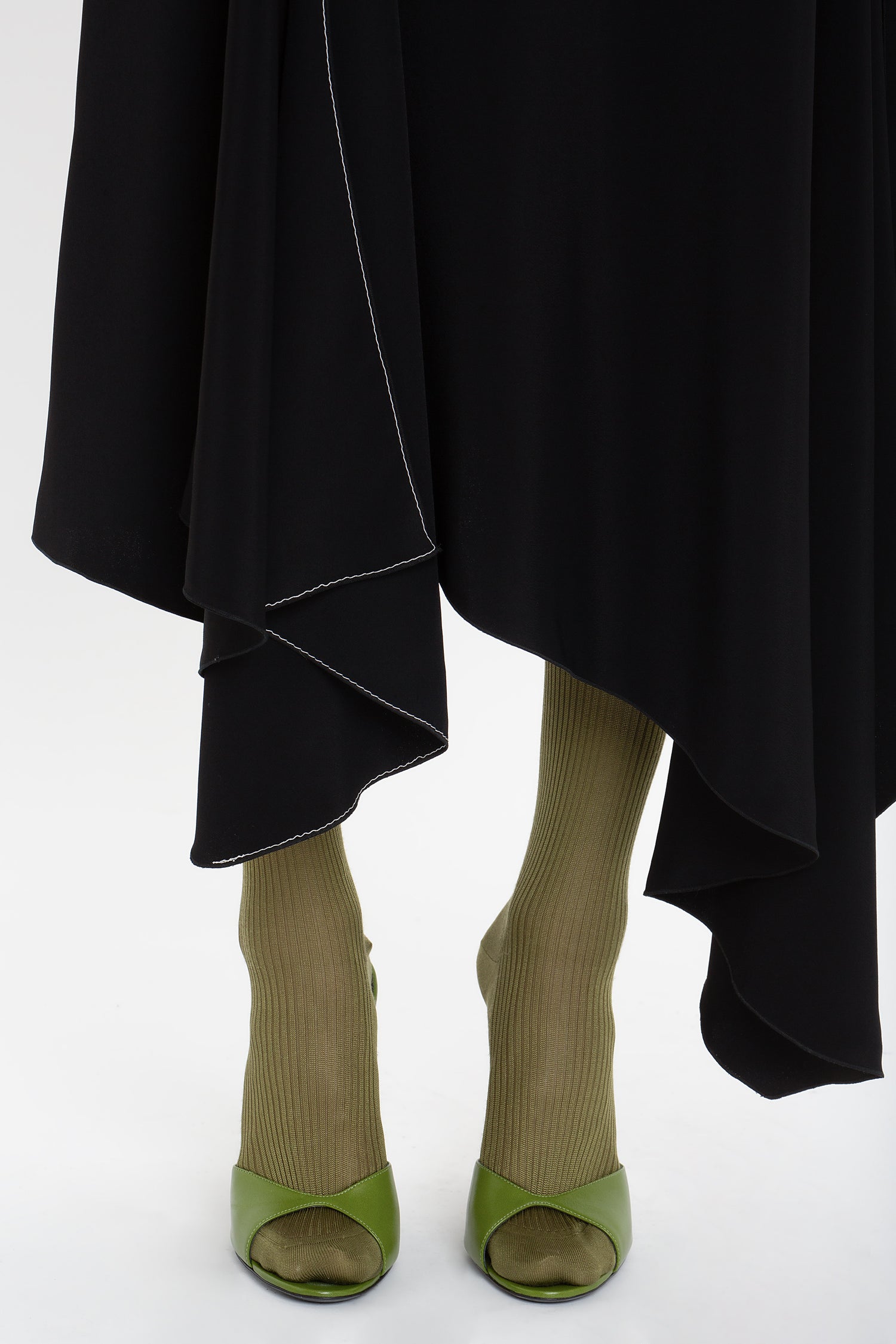 A person wearing olive green open-toed heels and ribbed olive green merino wool knit socks, with the Henley Shirt Dress In Black by Victoria Beckham cascading below the knees.