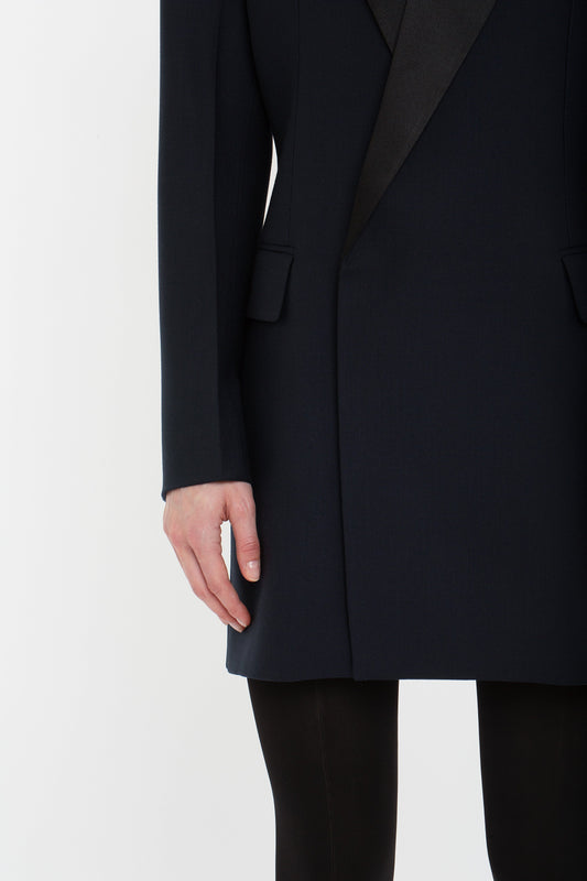 Close-up of a person wearing the Exclusive Fold Shoulder Detail Dress In Midnight by Victoria Beckham, standing against a white background. Their left hand is visible, resting casually by their side, reminiscent of the sophisticated elegance seen in Victoria Beckham’s designs.
