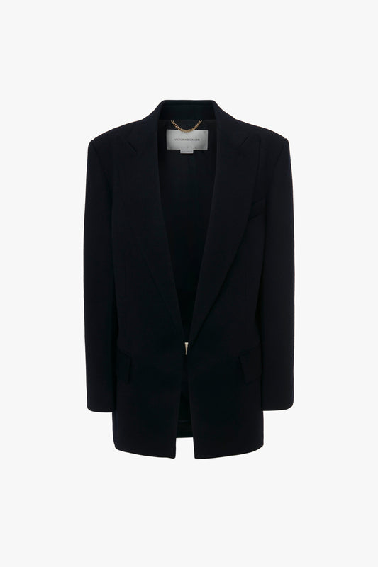 A sleek black blazer with a contemporary feel hangs on a hanger against a white background, reminiscent of Victoria Beckham's Peak Lapel Jacket In Midnight designs.