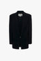 A sleek black blazer with a contemporary feel hangs on a hanger against a white background, reminiscent of Victoria Beckham's Peak Lapel Jacket In Midnight designs.