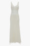 A long, off-white sleeveless dress with thin shoulder straps, a fitted bodice, and a flowing skirt. The Ruffle Detail Midi Dress In Ivory by Victoria Beckham features tactile lace detail on the bodice and a slight sheen to the fabric, epitomizing the charm found in elegant midi dresses.