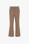 A pair of 1970s-inspired brown flared dress pants with a structured waistband, front seams, and a flattering hint of ankle at the bottom has been replaced with the Wide Cropped Flare Trouser In Tobacco by Victoria Beckham.