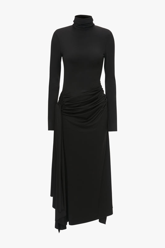 A black long-sleeve turtleneck top with a high neckline, paired with a High Neck Asymmetric Draped Dress In Black, designed in a form-fitting style, displayed against a white background by Victoria Beckham.