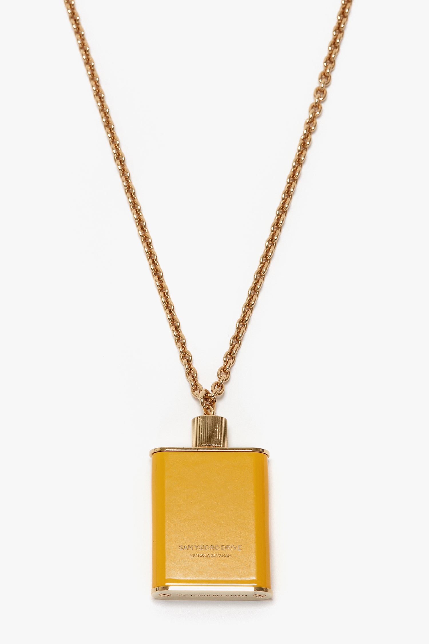 A gold-colored necklace featuring a small, rectangular pendant designed to resemble a flask in gold brushed brass. The pendant is inscribed with "San Ysidro Drive," "1947," and "Gold Label Reserva Especial." This unique jewellery piece exudes elegance, reminiscent of the Perfume Bottle Necklace In San Ysidro Drive by Victoria Beckham branding.