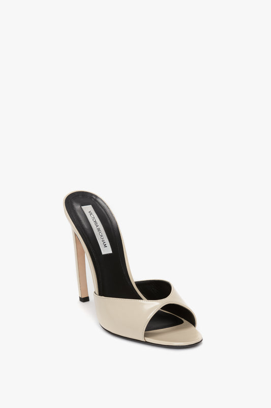 A single Classic Mule In Macadamia Calf Leather by Victoria Beckham, featuring a beige high-heeled sandal with black insole and open toe, a slim seductive curved heel, and a wide front strap.
