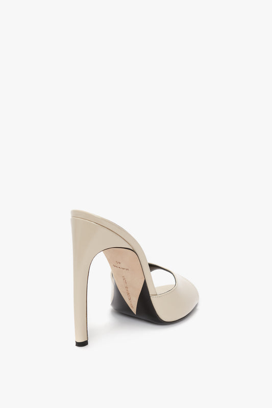 A single beige high-heeled shoe with an open back is showcased from the rear, featuring a seductive curved heel and crafted from luxury calf leather. This is the Classic Mule In Macadamia Calf Leather by Victoria Beckham.