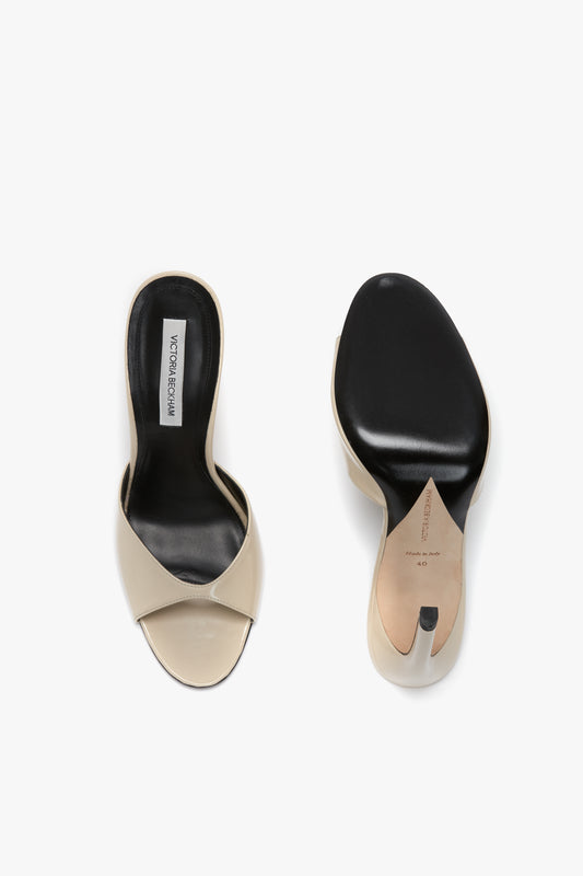 A pair of beige open-toe sandals with black insoles and a seductive curved heel. Crafted from luxury calf leather, the Victoria Beckham Classic Mule In Macadamia Calf Leather is shown from the top, highlighting its flattering toe cleavage, while the other displays the sole.