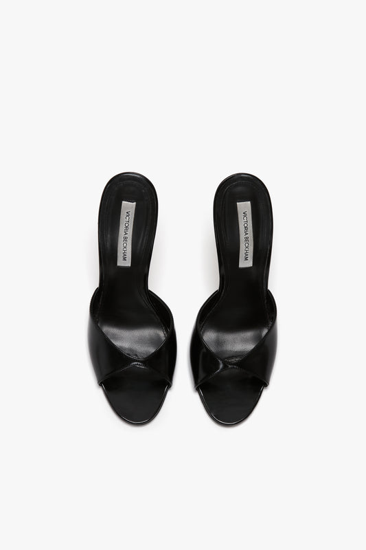 A pair of black open-toe high-heeled sandals with crossed straps, crafted from luxury calf leather, and a label inside reading "Victoria Beckham Classic Mule In Black Calf Leather.