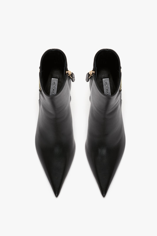 A top-down view of a pair of the Victoria Beckham Pointed Toe Half Boot In Black Soft Calf Leather, featuring side zippers and a brand label visible inside each shoe.