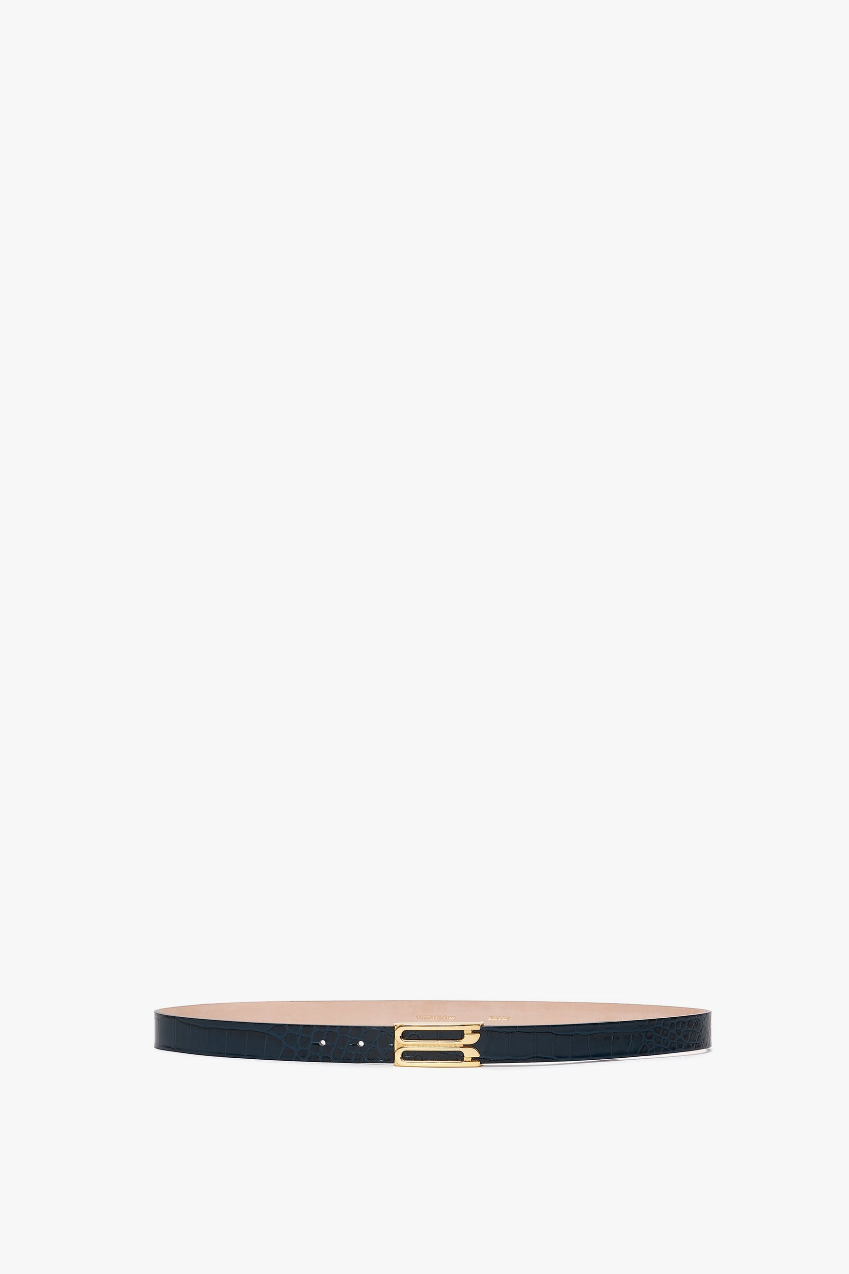 A slim, midnight blue belt crafted from croc-embossed calf leather, featuring a striking gold buckle, displayed against a white background has been replaced with the **Frame Belt In Midnight Blue Croc Embossed Calf Leather by Victoria Beckham**.