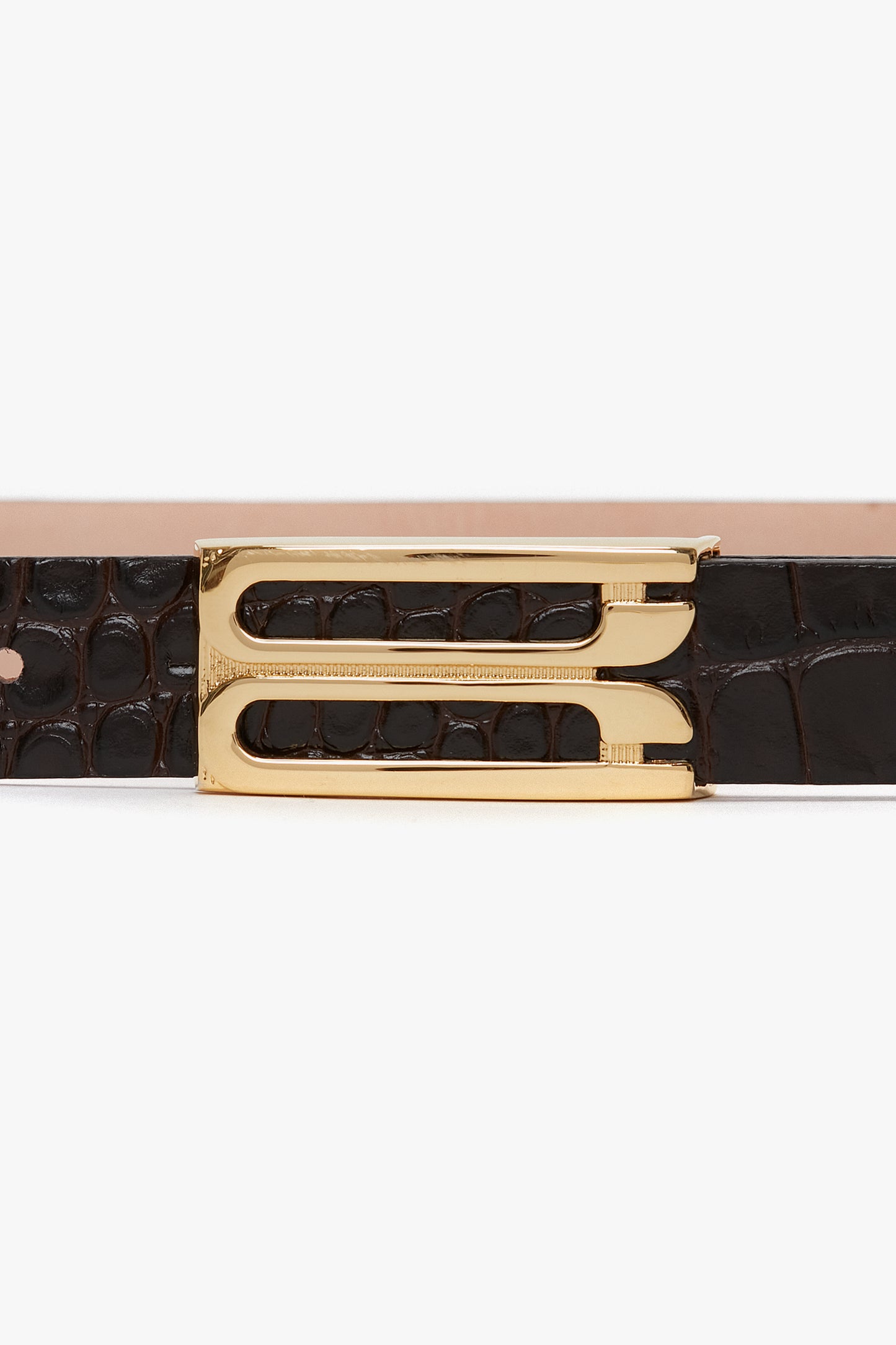 A close-up image of a Frame Belt In Espresso Croc Embossed Calf Leather made from black croc-embossed calf leather, featuring a gold-toned buckle with unique dual-prong design by Victoria Beckham.