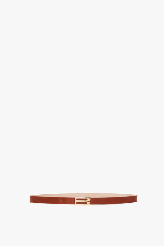 A thin, Exclusive Frame Buckle Belt in tan leather with gold hardware, centered and isolated on a white background by Victoria Beckham.