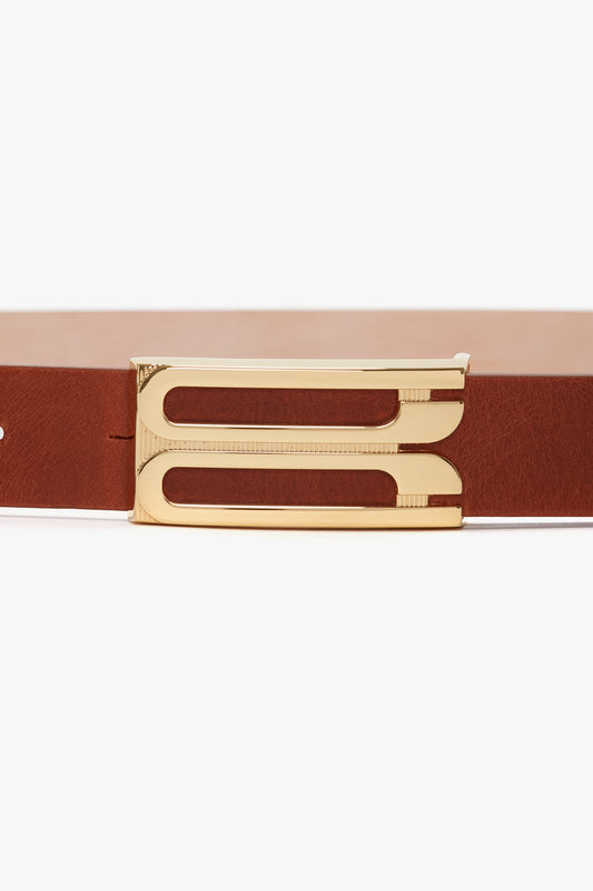 Close-up of a Victoria Beckham Exclusive Frame Buckle Belt In Tan Leather with shiny gold hardware on a white background.
