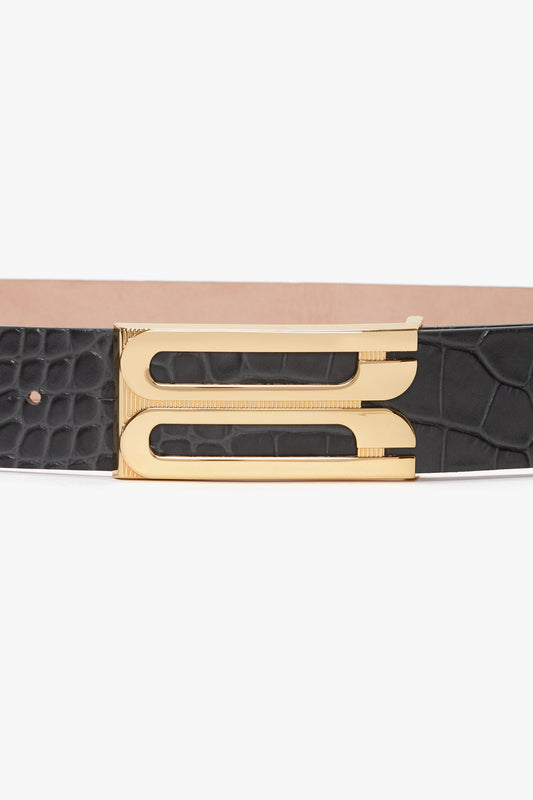 A Jumbo Frame Belt In Slate Grey Croc Embossed Calf Leather by Victoria Beckham with a gold rectangular buckle featuring a cutout design, showing a textured pattern on the leather.