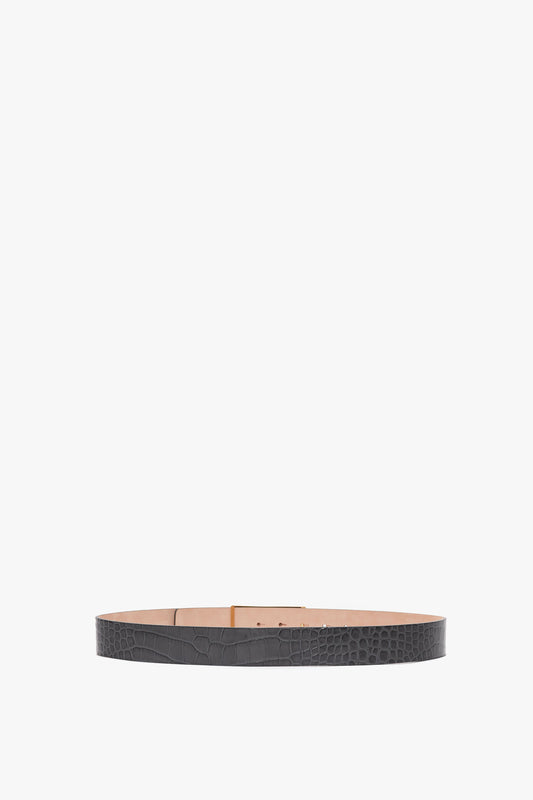 A thin, Jumbo Frame Belt In Slate Grey Croc Embossed Calf Leather by Victoria Beckham with a tan interior, laid flat in a circular shape against a white background.