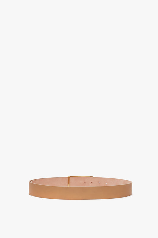 A minimalistic tan leather belt crafted from smooth calf leather, featuring a rectangular gold buckle. The Jumbo Frame Belt In Camel Leather by Victoria Beckham is elegantly displayed on a plain white background, making its refined gold hardware stand out.