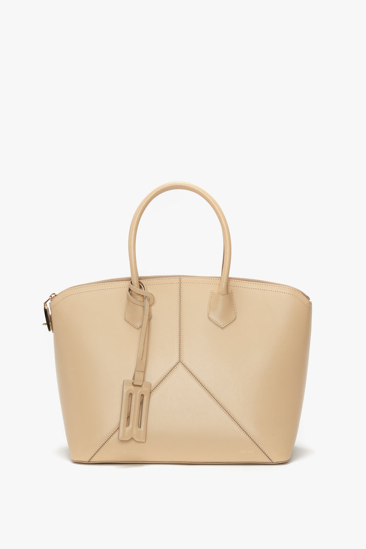 Victoria Beckham Victoria Bag In Sesame Leather: Beige leather handbag with dual handles and minimalist stitching, featuring a small attached tag and sleek leather panels.