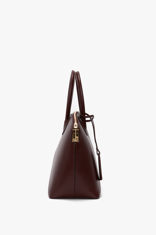 Side view of a Victoria Beckham Victoria Bag In Burgundy Leather featuring double handles, an adjustable strap, and a gold zipper closure.
