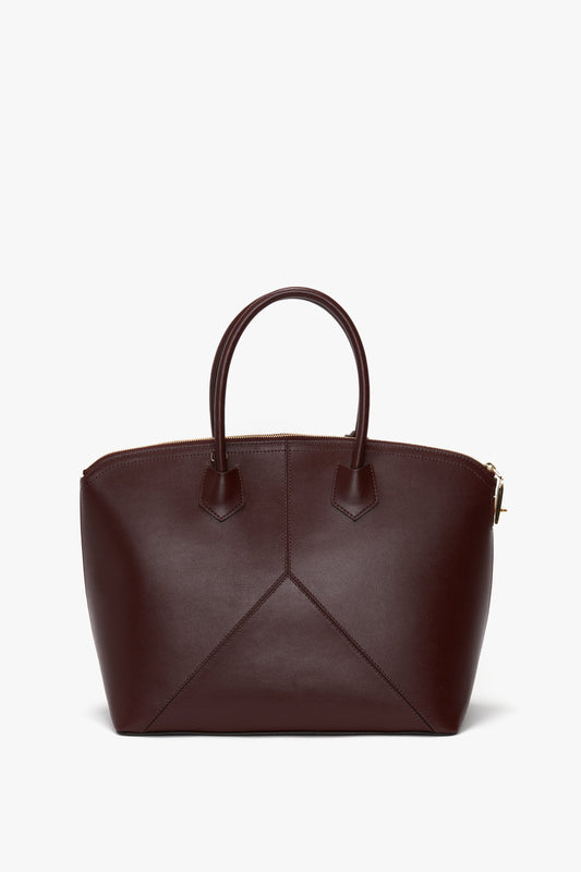 A dark brown leather Victoria Beckham Victoria Bag In Burgundy Leather with a structured shape, two short handles, and a visible seam design on the front; features an adjustable strap for versatile carrying.