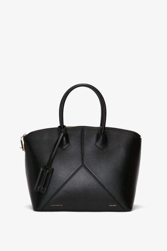 A Victoria Beckham Victoria Bag In Black Leather with structured leather panels, two top handles, and a zipper closure.