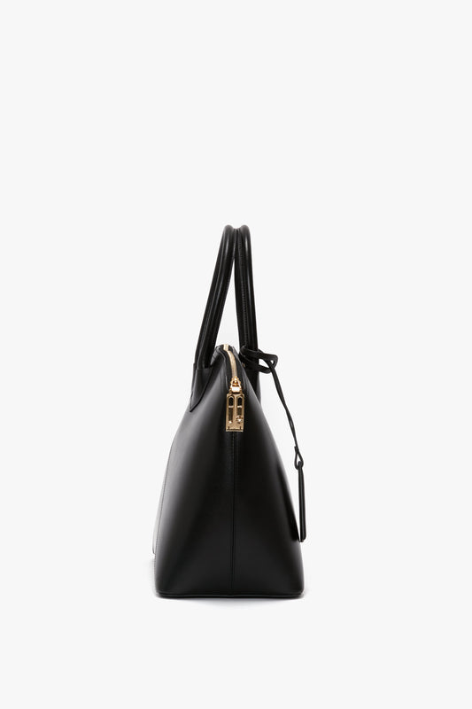 Side view of a black leather Victoria Bag In Black Leather with gold hardware and double handles, against a white background from Victoria Beckham.