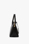 Side view of a black leather Victoria Bag In Black Leather with gold hardware and double handles, against a white background from Victoria Beckham.