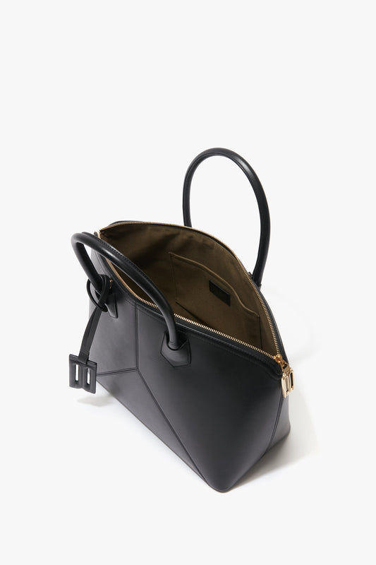 A black leather Victoria Beckham Victoria Bag In Black Leather with gold zipper detailing and double handles, showing its open interior lined with brown fabric.