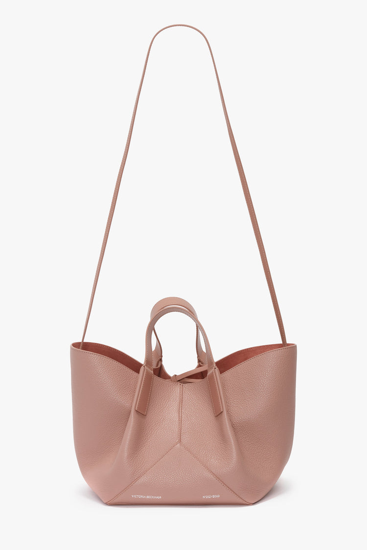 Introducing the W11 Mini Tote Bag In Marshmallow Leather by Victoria Beckham: a blush pink crossbody handbag with long and short straps, featuring a beautifully textured structured calf leather finish.
