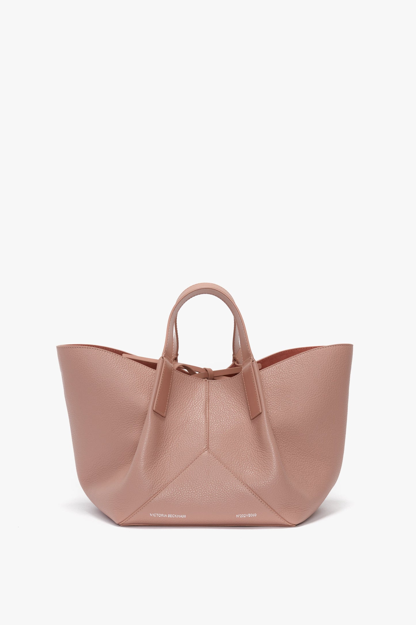 A blush pink Victoria Beckham W11 Mini Tote Bag In Marshmallow Leather, crafted from structured calf leather, features short handles and a spacious, wide-open design displayed on a white background.