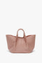 A blush pink Victoria Beckham W11 Mini Tote Bag In Marshmallow Leather, crafted from structured calf leather, features short handles and a spacious, wide-open design displayed on a white background.