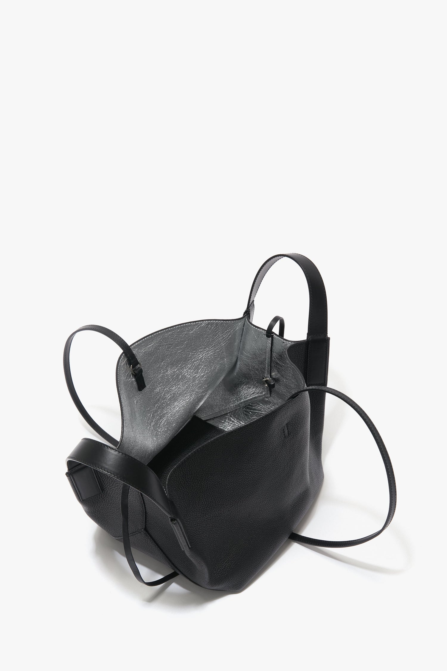 A black leather W11 Mini Tote Bag In Black Leather crafted from grainy calf leather by Victoria Beckham with an open top, revealing a gray interior and long, thin shoulder straps for a touch of luxurious sophistication.