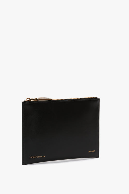 Black Victoria Beckham B Frame Pochette In Black Leather clutch with a gold zipper, isolated on a white background.