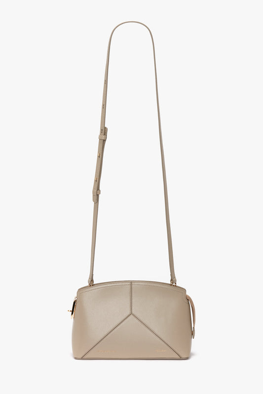A Victoria Crossbody Bag In Taupe Leather with an adjustable and removable strap and gold-tone hardware, featuring a geometric design on the front, exemplifying Victoria Beckham leather goods craftsmanship.