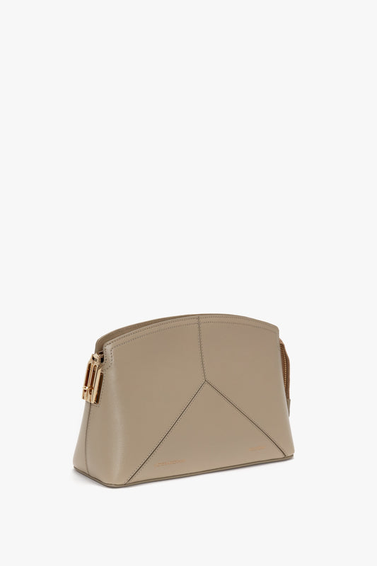 A Victoria Beckham Victoria Crossbody Bag In Taupe Leather with a gold buckle on one side is shown against a white background, featuring an adjustable and removable strap for versatile styling.