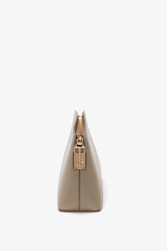 A side view of a Victoria Beckham Victoria Crossbody Bag In Taupe Leather with gold hardware on the closure, set against a white background. It features an adjustable and removable strap for versatile styling.