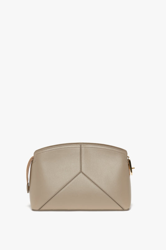 A beige leather handbag with a unique geometric design on the front, featuring a top zipper and an adjustable and removable strap with a golden clasp. This Victoria Beckham Victoria Crossbody Bag In Taupe Leather effortlessly transitions from a stylish handbag to a chic calf leather crossbody bag.