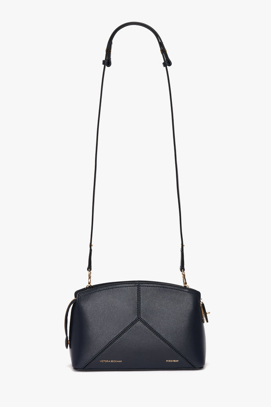 A black leather crossbody bag with gold accents, a thin adjustable shoulder strap, and geometric stitching on the front. This exquisite piece of leather goods features a top zipper closure and exudes elegance akin to the Exclusive Victoria Crossbody Bag In Navy Leather by Victoria Beckham.