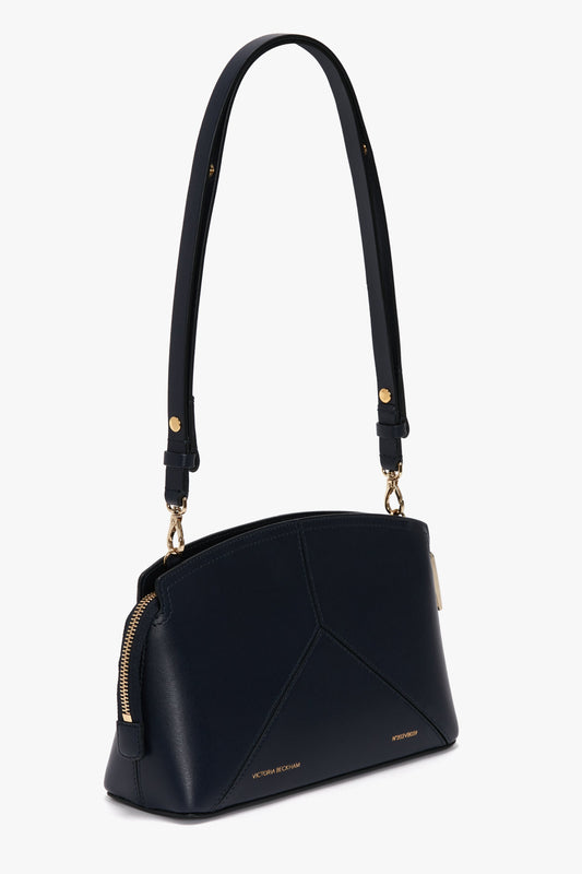An Exclusive Victoria Crossbody Bag In Navy Leather by Victoria Beckham, featuring gold hardware, a structured design, a single shoulder strap, and embossed brand logos on the front.