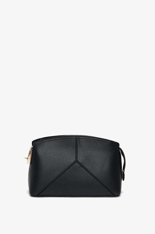 A small black Victoria Crossbody Bag In Black Leather with a minimalist design, crafted from textured calf leather by Victoria Beckham, featuring a gold zipper detail on the left side.