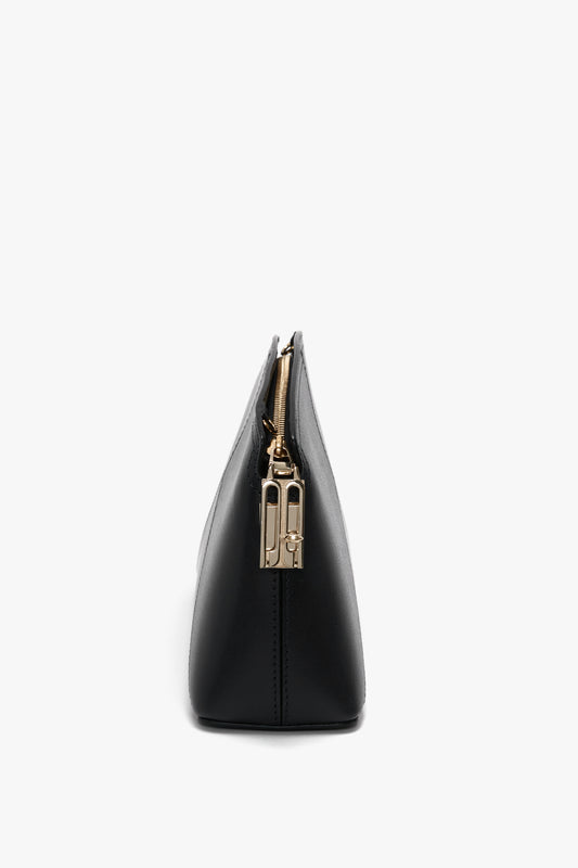 Side view of a black zippered Victoria Beckham Victoria Crossbody Bag In Black Leather, made from textured calf leather with gold hardware and an adjustable strap, against a white background.