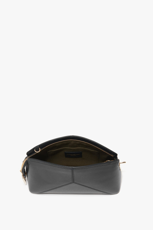 A Victoria Beckham Victoria Crossbody Bag In Black Leather with an adjustable strap and gold zipper is shown open, displaying an olive green interior lining crafted from textured calf leather.