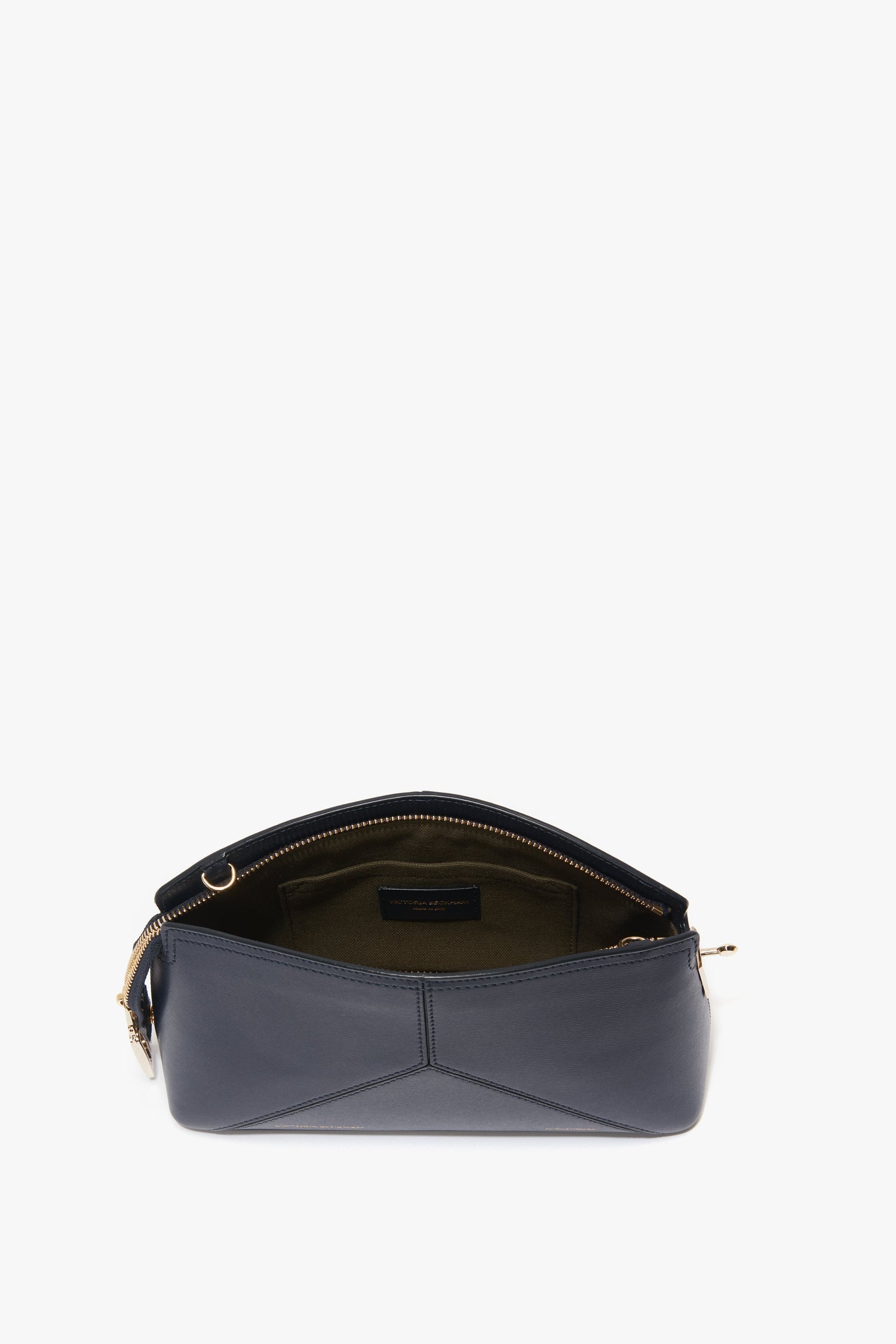 A black leather handbag is shown with its zipper open, displaying an empty beige interior. The Exclusive Victoria Crossbody Bag In Navy Leather by Victoria Beckham, a fine piece of leather goods, features gold hardware and a structured shape reminiscent of a sophisticated clutch bag.