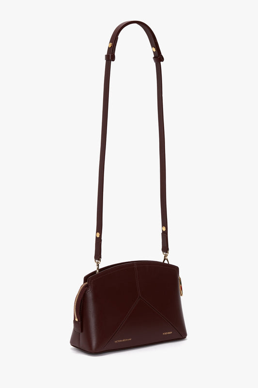 A Victoria Beckham Victoria Crossbody Bag In Burgundy Leather features adjustable straps, a gold zipper, and a sophisticated padlock closure.