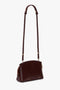 A Victoria Beckham Victoria Crossbody Bag In Burgundy Leather features adjustable straps, a gold zipper, and a sophisticated padlock closure.